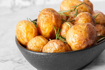 Roasted whole baby potatoes with rosemary in a black stoneware dish. On a marble background