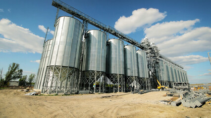 Industrial grain silos under blue sky. A row of large industrial metal grain silos standing in a dirt field under a clear blue sky with scattered clouds. © Iryna
