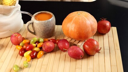 Bright pumpkin beverage inside ceramic mug beside large pumpkin, fruits scattered across bamboo mat, colorful autumn harvest scene showcasing natural produce and rustic textures with cozy aesthetic.