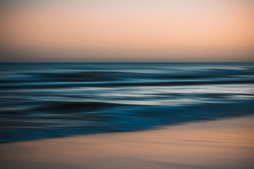 Blurred ocean waves under a soft orange and blue sky at dusk.