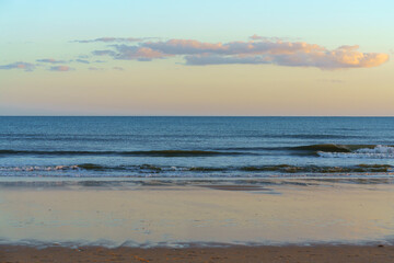 Calm ocean waves gently reaching the sandy shore under a soft pastel sky.