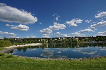 A beautiful summer landscape with a pond, on the mirror surface of which the blue sky with white clouds is reflected.