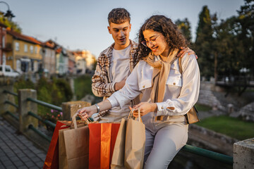 couple sit near river with shopping bags after successful shopping