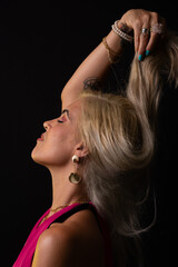 Fototapeta premium Beautiful Caucasian woman in red dress posing and touching her blonde hair. Isolated on black background. Salvador, Bahia.