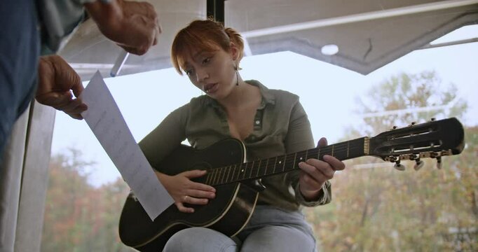 A woman engages in a private music lesson, practicing acoustic guitar with her male teacher, focusing intently as he offers guidance and feedback to refine her skills.