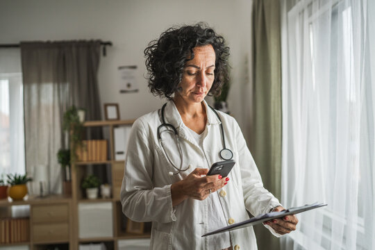 mature woman doctor stand and take a photo of clipboard with cellphone
