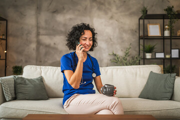 Obraz premium mature woman doctor sit on sofa and talk on mobile phone at home