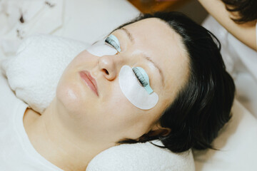 Girl cosmetologist laminates and paints woman eyelashes