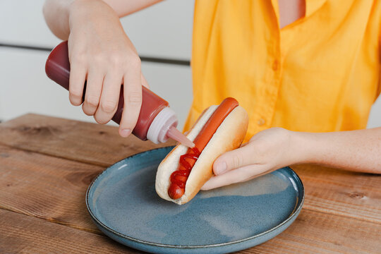 Person Squeezing Ketchup on Hot Dog in Bun