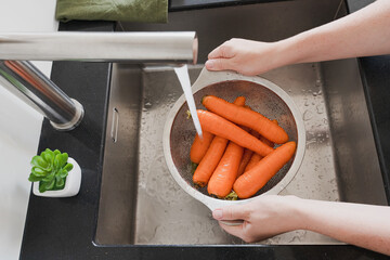 Hands Washing Carrots In Colander Under Running Water