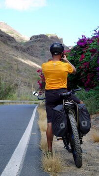 Departure on asphalt road with electric mountain bike after a short stop to drink and take pictures of the landscape. The cyclist wears a protective helmet