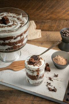 Chocolate brownie trifle bowl with ingredients on white tray in a rustic kitchen.