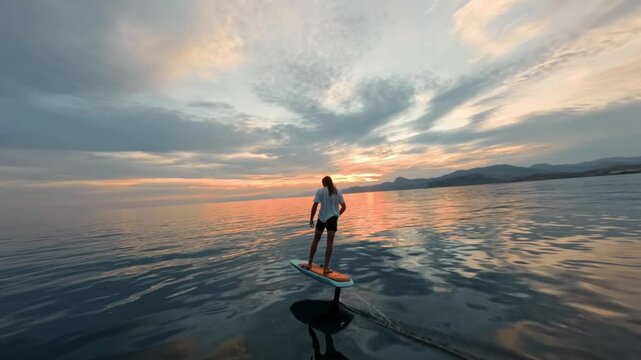 Man glides on hydrofoil board on water surface of sea against the background of beautiful golden sunset sky. High quality FullHD footage