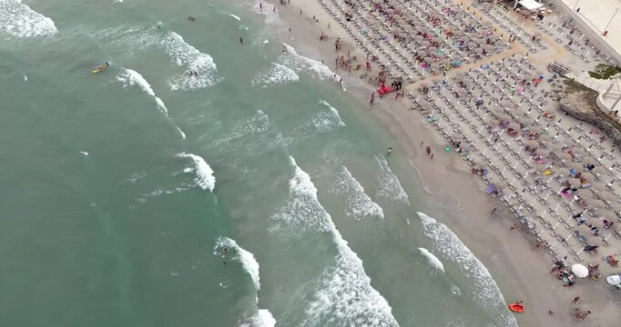 Aerial view of a beach club on the sandy coast of San Foca in the province of Lecce, Salento, Puglia, Italy. There are people in the water despite the rough sea.