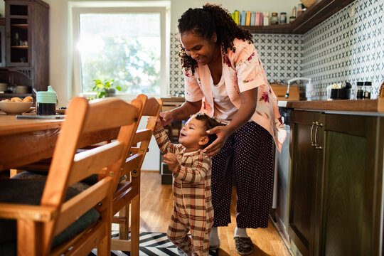 Mother helping toddler take first steps in the kitchen
