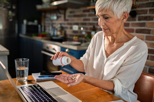 Senior woman taking supplements while working from home on a laptop
