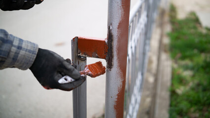 Male hand painting metal fence with a brush with red oxide metal primer