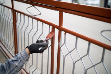 Male hand painting metal fence with a brush with red oxide metal primer
