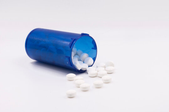 A close up image of several small white pills spilling out of a blue pill bottle onto a white background. 