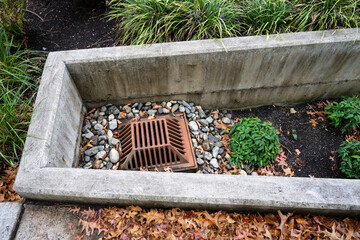 Rusty raised square iron stormwater drain surrounded by small rocks and plants, lower than ground...