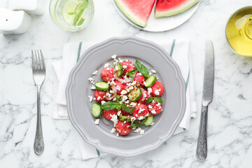 Delicious watermelon salad with feta cheese, vegetables and spices served on white marble table, flat lay