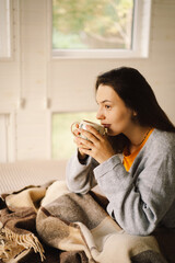 A woman relaxes in a bright, serene room, sipping coffee while focused on her book. The natural...