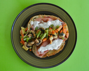 Toasted sourdough ciabatta bread with prosciutto, tzatziki and pan fired vegetables on a plate.