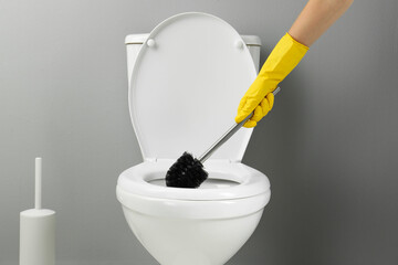 Woman cleaning toilet with brush in bathroom, closeup