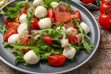 Tasty salad with arugula, mozzarella cheese, tomatoes and jamon on wooden table, closeup