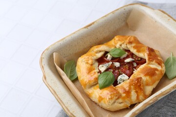 Tasty galette with tomato, basil and cheese on white tiled table, closeup