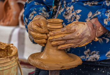 Close up of pottery or ceramic artwork in a wheel. Old woman's hands working with mud and building ceramic. Colorful dress.
