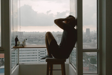 Introvert lonely asian man sitting at the windows enjoy being alone in apartment.