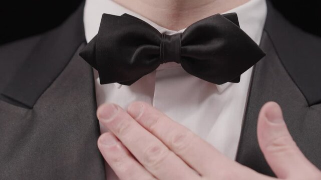 Close-up of Hands Adjusting Black Bow Tie: Formal Event Preparation Detail | Elegant Man's Neck in White Collar and Tuxedo | Gentleman Getting Ready Scene with Classic Neckwear