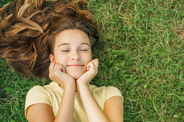 Close up top view high angle photo beautiful young girl child dreamily closed eyes her hands on cheeks natural background green grass