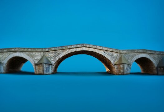 An old stone bridge with three arches against a bright blue sky.