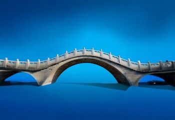 A stone arch bridge spans a serene blue body of water, reflecting the clear sky above.