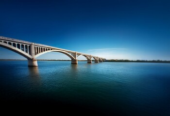 A concrete bridge arches over a calm body of water, with a deep blue sky above.