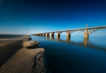 Fototapeta premium A steel bridge spans a calm body of water with a clear blue sky overhead.