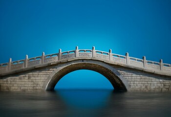 Fototapeta premium A stone arch bridge with intricate carvings on the railing crosses over a calm body of water.