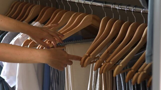 Women's hands choose trousers and jeans in the wardrobe. Clothes neatly hung in the closet. Concept storage and order 
