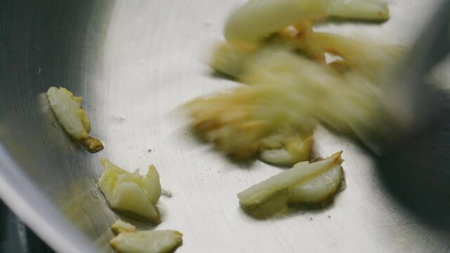 Golden brown pieces of garlic being stirred with spatula in sizzling oil in frying pan. Extreme close-up shot