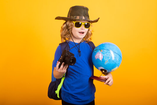 Kid tourists with backpacks and camera hold world globe isolated on yellow studio background. Child boy with backpacks exploring world and environment. Studio portrait on a yellow background.