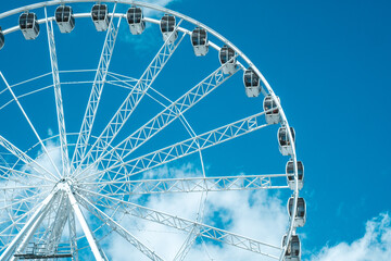 A towering ferris wheel stands against a blue sky with fluffy clouds during a bright afternoon © reddish