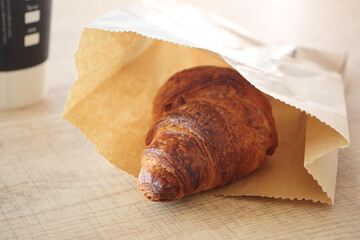 A Freshly Baked, Delightfully Flaky Croissant Wrapped in a Classic Brown Paper Bag