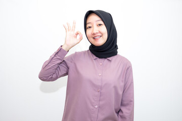 portrait of Indonesian Asian woman wearing shirt and hijab showing ok sign with one hand on eyes looking at camera through fingers. giving sign of agreement. Isolated on white Background