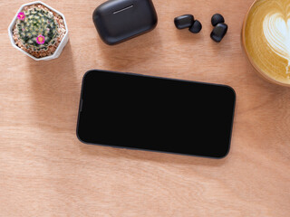 Top view composition, concept online shopping, blog, logo, product, and social media. Black screen smartphone mockup on wooden background and coffee cup, Bluetooth headphones..