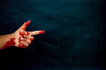 A bloody hand forming a gun gesture against a dark background with copy space, symbolizing violence and threat © Anzz Stock