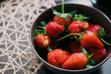 On a wooden table, there is a lovely bowl filled with fresh, ripe strawberries, their vibrant red color complemented by lush green leaves