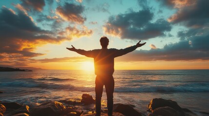 A man stands on a beach with his arms outstretched, looking up at the sky