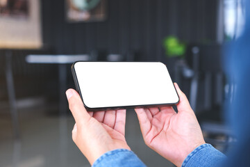 Mockup image of a woman holding and using mobile phone with blank desktop in cafe